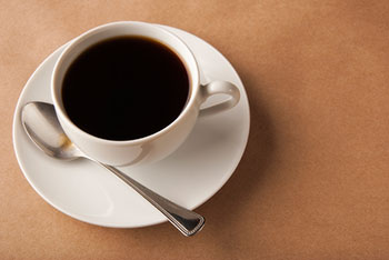 A cup of black coffee served on a saucer with a spoon alongside