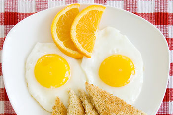 a breakfast meal of fried eggs and toast garnished with a slice of orange