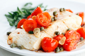 A piece of roasted halibut topped with cherry tomatoes, sliced garlic, and capers