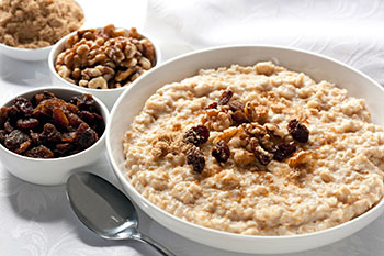 a bowl of cooked oatmeal garnished with brown sugar, nuts, and raisins