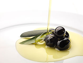 olive oil being drizzled over a spray of olive leaves and black olives