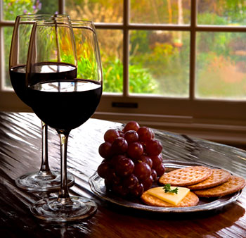 two wineglasses containing red wine next to a plate of grapes, cheese, and crackers