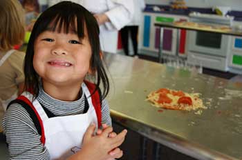 An Asian child smiling at her role in making pizza in a professional kitchen