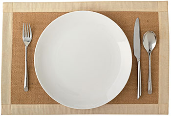 a place setting of fork, knife, spoon, and dinner plate on a placemat