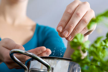 a woman sprinkling salt into a saucepan