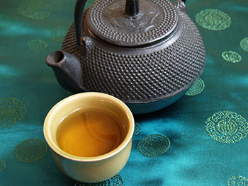 a cup of green tea next to a traditional iron teapot