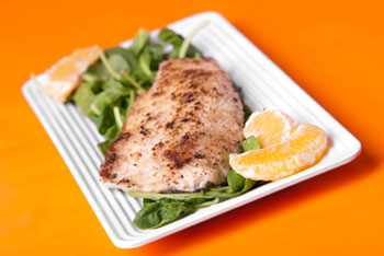 a filet of seared trout on a bed of greens, garnished with orange slices