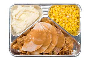 old-fashioned TV dinner in an aluminum tray: processed turkey slices with dressing, mashed potatoes, and corn