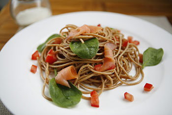 a meal of whole wheat spaghetti with smoke salmon, chopped tomatoes, and basil leaves