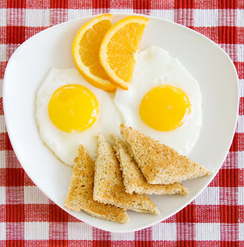two fried eggs sunny-side-up with a piece of toast, garnished with orange slices