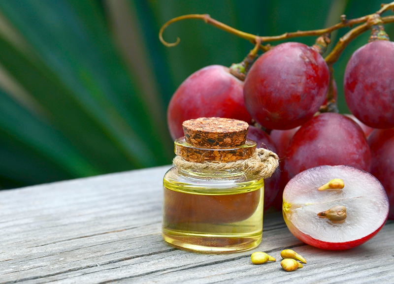 grapes cut in half to expose the seeds alongside a vial of grapeseed oil