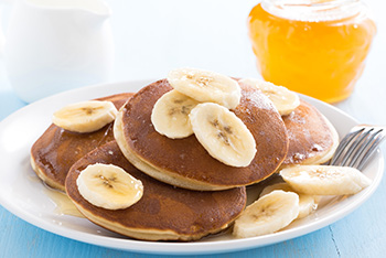 pancakes topped with fresh sliced bananas and accompanied by a glass of orange juice
