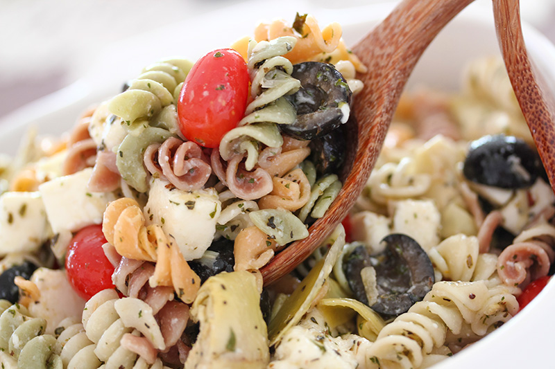 a pasta salad with rotini pasta, black olives, tomatoes, and blue cheese