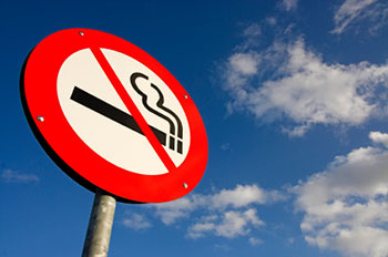 a no smoking sign against a blue sky with a few fluffy white clouds