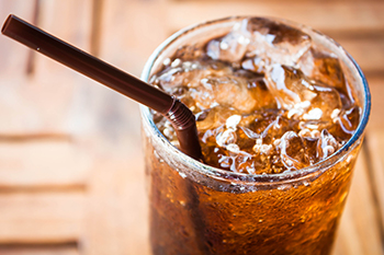 a glass of cola with ice and a straw