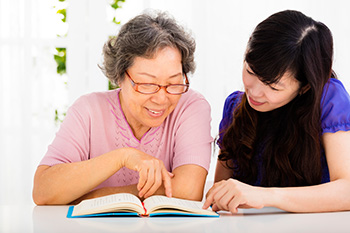 two Asian persons, one older, one younger, appear to be discussing a book one holds open on a table