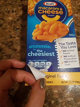 a box of Kraft mac and cheese with a hand removing a sticker over the sodium, calories, and other information on the front of the box