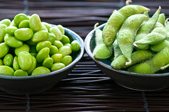 A bowl of soybeans and a bowl of edamame pods