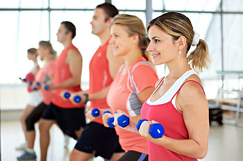 A smiling woman using dumbbells while participating in an exercise class