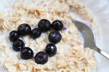 A closeup of a bowl of oatmeal topped with blueberries arranged in the shape of a heart
