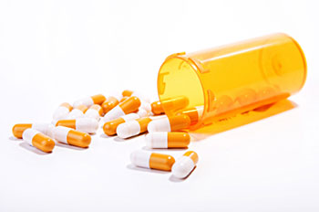 A prescription bottle with pill capsules spilling out of it