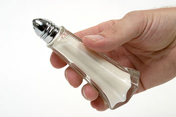 a hand holding a glass salt shaker full of salt
