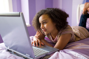 an adolescent lying on a bed using a laptop computer