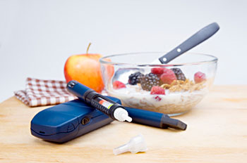 an insulin injector and glucose monitor placed next to a bowl of high-fiber cereal topped with blackberries and raspberries