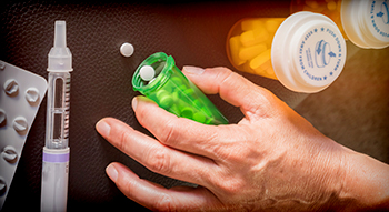 a person's hand holding a bottle of pills alongside an insulin injector
