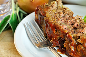 a slice of meatloaf on a white plate with a fork alongside, ready to eat with