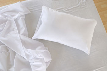 an unmade bed with a single standard sized pillow on it