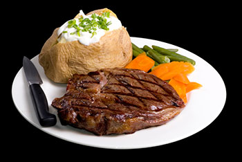 Steak with a baked potato and a side of green beans and carrots