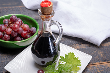 a glass bottle of balsamic vinegar next to a small bowl of red grapes