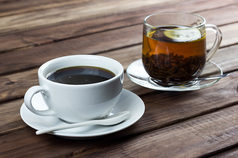 a cup of hot black coffee and a cup of hot black tea on a rustic wooden table