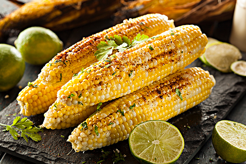 a plate of several ears of cooked corn garnished with pats of butter