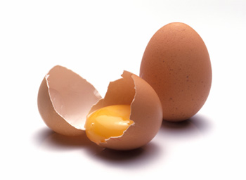 one whole brown egg and one brown egg that has been cracked open, with the yolk of the egg remaining in the egg's cup