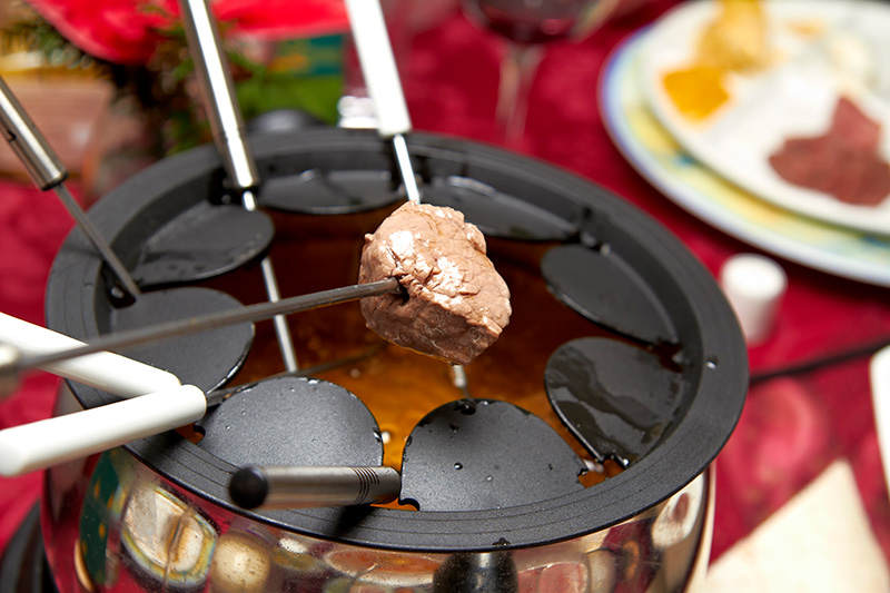 A fondue pot filled with oil - a cube of meat is held on a fondue fork, ready for dipping