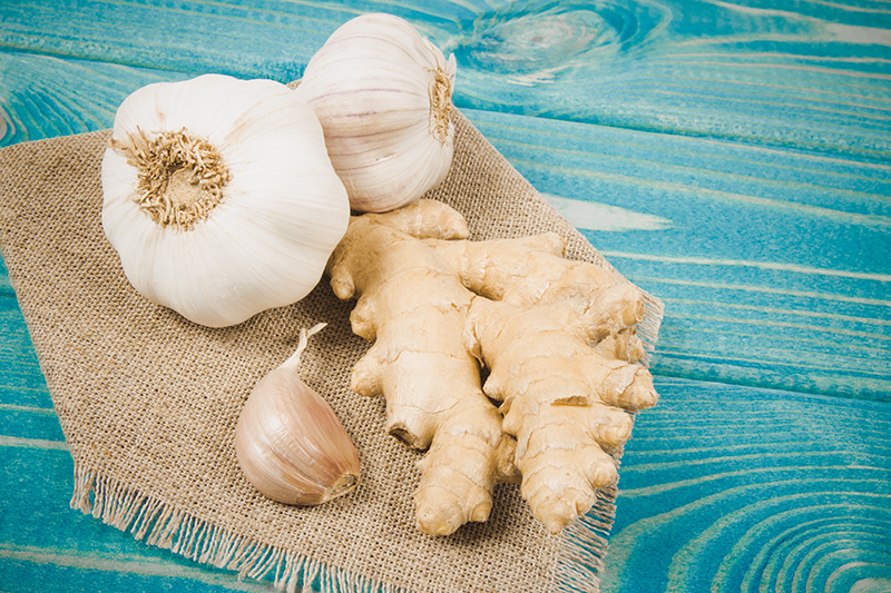 Fresh garlic bulb, a single garlic clove, and a knob of fresh, unpeeled ginger on a wooden table