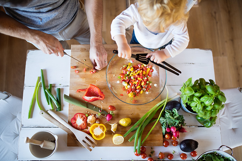 an overhead view of a parent and child cutting vegetables at a wooden table