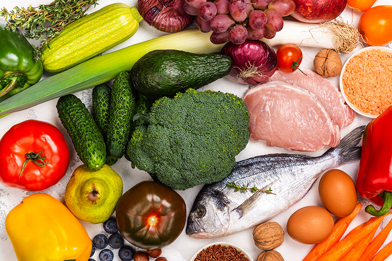 elements of a Mediterranean diet, including fruits, vegetables, fish, lean meats, legumes, and whole grains, on a white background