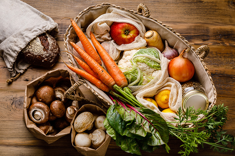 a variety of fruits and vegetables in a carrying basket with a loaf of rustic bread