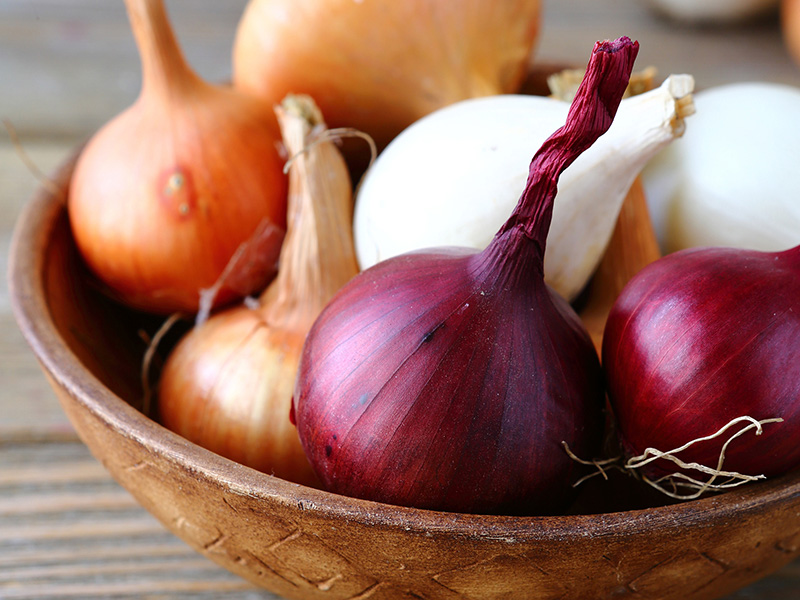 a variety of onions in a wooden bowl