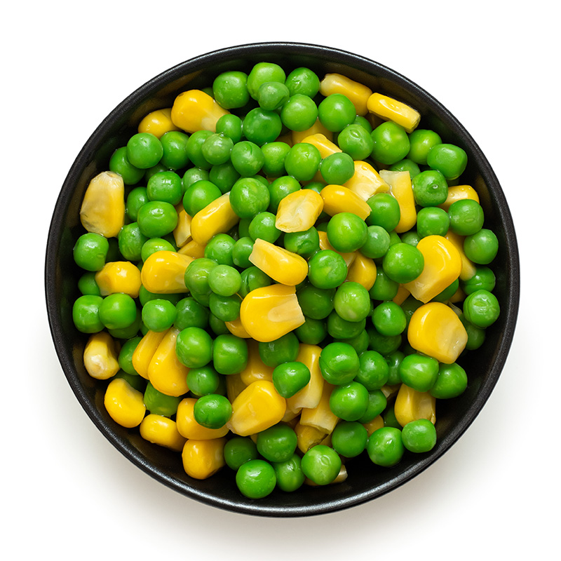 fresh peas and corn in a black bowl against a white background