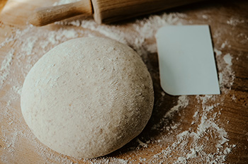 a ball of pizza dough on a wooden cutting board dusted with flour