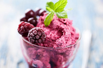 A parfait glass of raspberry sorbet garnished with frozen raspberries and a sprig of mint