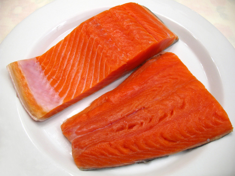 Two filets of uncooked sockeye salmon on a white plate