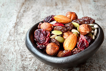 a bowl of trail mix that includes nuts, seeds, and dried fruit, a good snack for those with Cystic Fibrosis