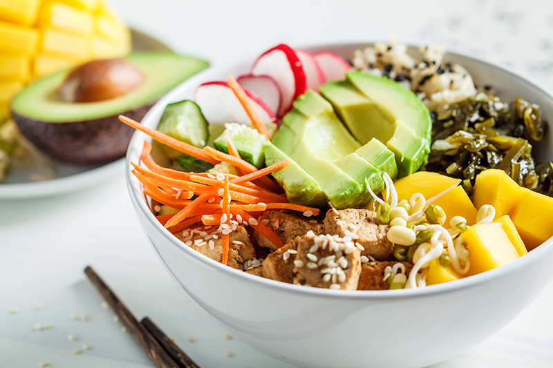a vegan poke bowl of tofu, carrots, seaweed, mango, avocado, radishes, and brown rice