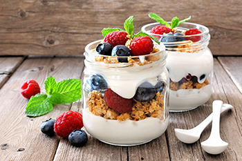 a parfait of yogurt, granola, blueberries, and raspberries in a clear glass jar
