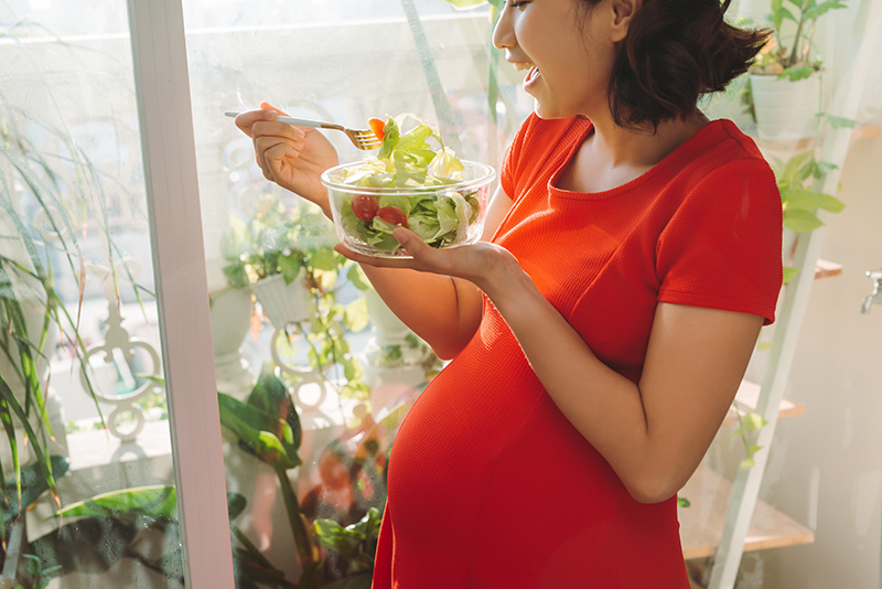 an Asian woman who is pregnant eating a fresh green salad